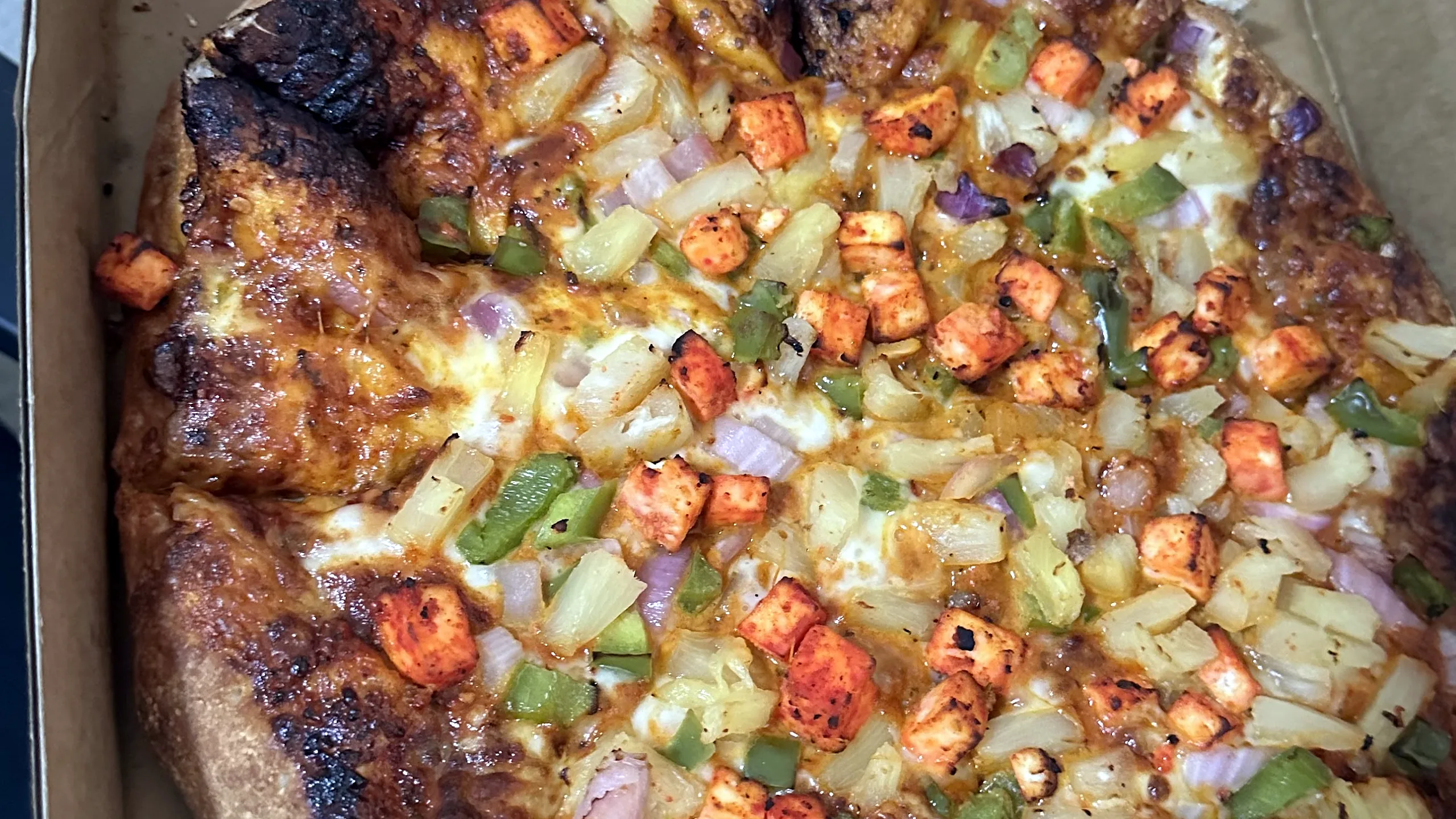 Well-done pizza with tandoori-spiced toppings, pineapple and peppers in a pizza box